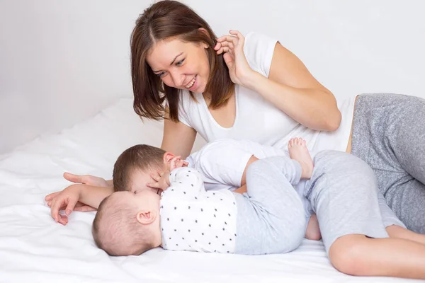 Young mom with her 5 year old son and 4 months old baby playing on a bed