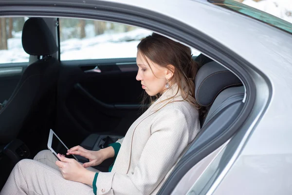 Attractive executive female manager working with a tablet in a backseat of a car