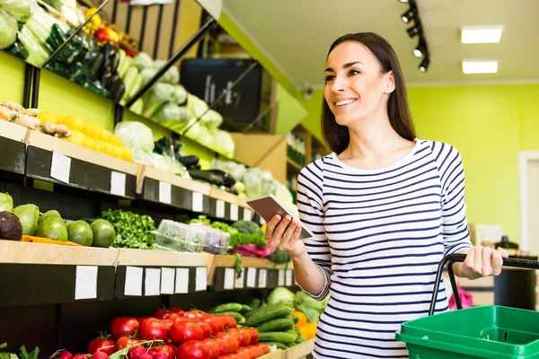 woman holding smartphone and checking buying list in supermarket