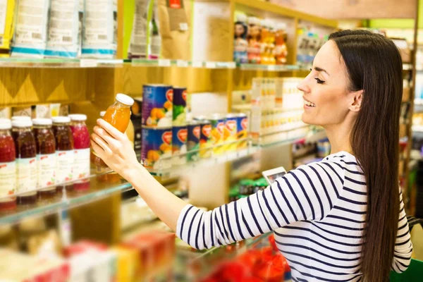 Gülümseyen Genç beyaz kadın süpermarkette raflardan ürünler seçme