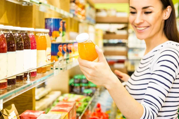 年轻的白种女人微笑从货架上选择超市的产品 — 图库照片