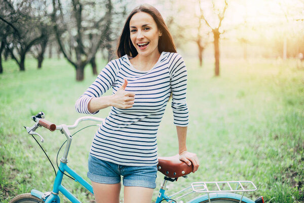 Young woman standing with bike and showing thumb up 