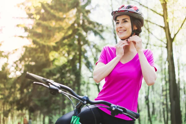 Happy young caucasian woman in helmet riding sport mountain bicycle in forest