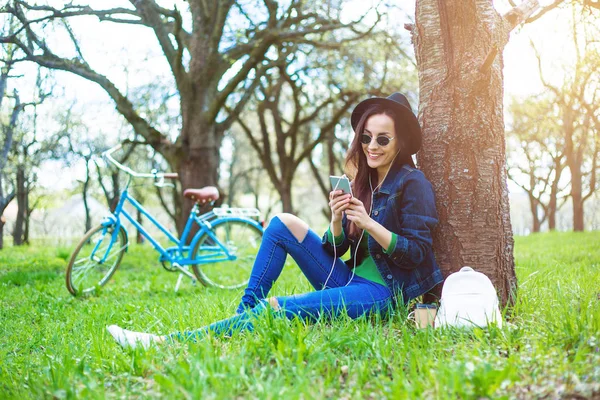 Случайная Женщина Солнцезащитных Очках Шляпе Сидит Траве Слушает Музыку — стоковое фото