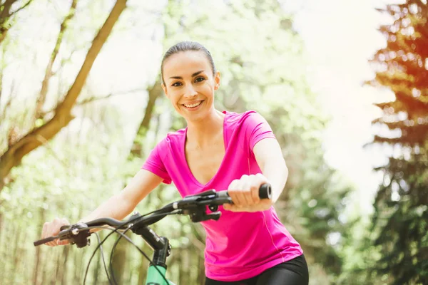 微笑年轻的白种妇女骑体育山地自行车在森林里 — 图库照片