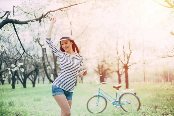 Young woman listening music and dancing outdoor with bike on background