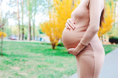Parlak yeşil ve sarı ağaçlar ve çim zemin üzerine bej ince elbise holding bel bölgende genç kadın yan görünüm
