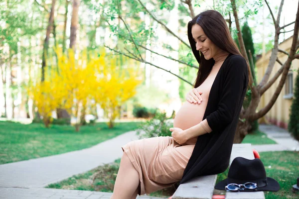 孕妇坐在长凳上 抱着肚子在公园里享受时光 — 图库照片