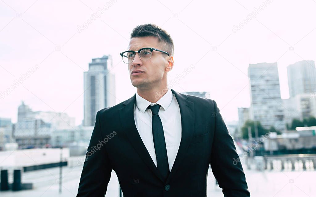 Determined young businessman in glasses on modern city background