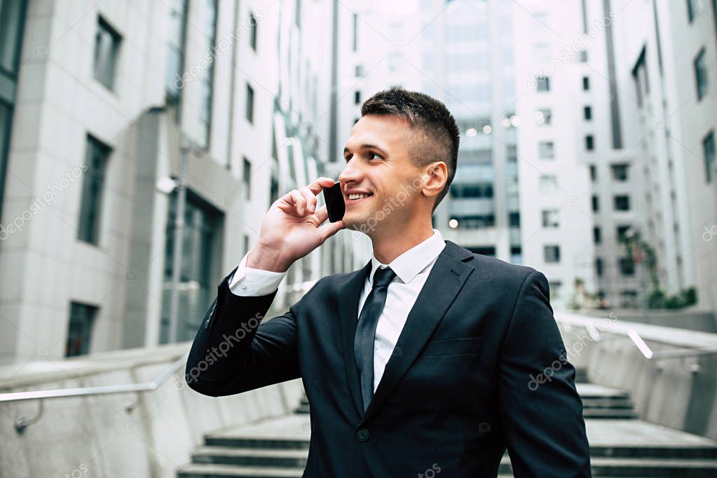 Young cheerful businessman using smartphone on modern city background
