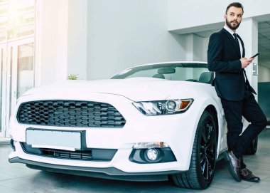 siyah elbiseli Bayilik, tam uzunlukta yeni modern car yakınındaki smartphone ayakta tutan yakışıklı adam