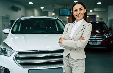 Takım elbise ayakta Bayilik araba arka plan üzerinde çapraz silah ile güzel gülümseyen pazarlamacı