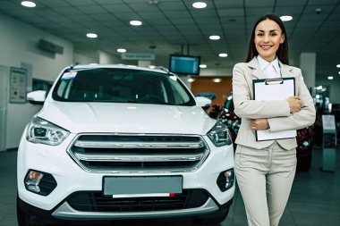 Takım elbise ayakta Bayilik araba arka plan üzerinde belgeleri ile güzel gülümseyen pazarlamacı