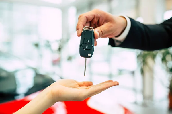 woman  receiving key of new car from salesman in dealership, close up of hands