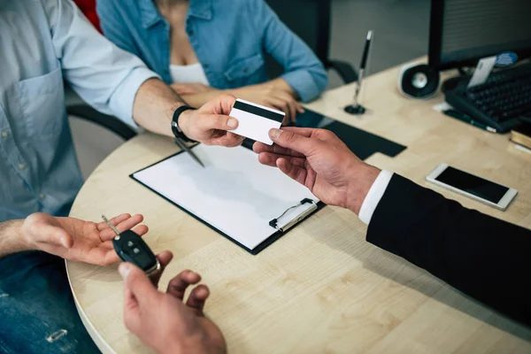 Cropped photo of Payment operation, male hands with credit card and key over desk in dealership