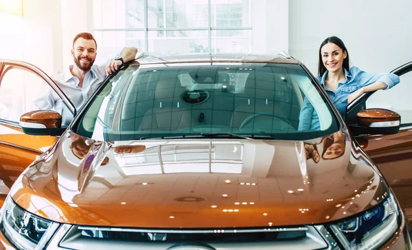 カジュアルで幸せな若いカップルが車のコンセプトを購入ディーラーで新車近くに立っているを着用します — ストック写真