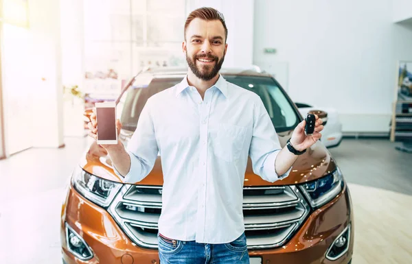 Mutlu yakışıklı adam araba anahtarı ve araba arka planda Bayilik smartphone ile ayakta