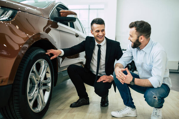 Male consultant and customer checking car details in dealership 