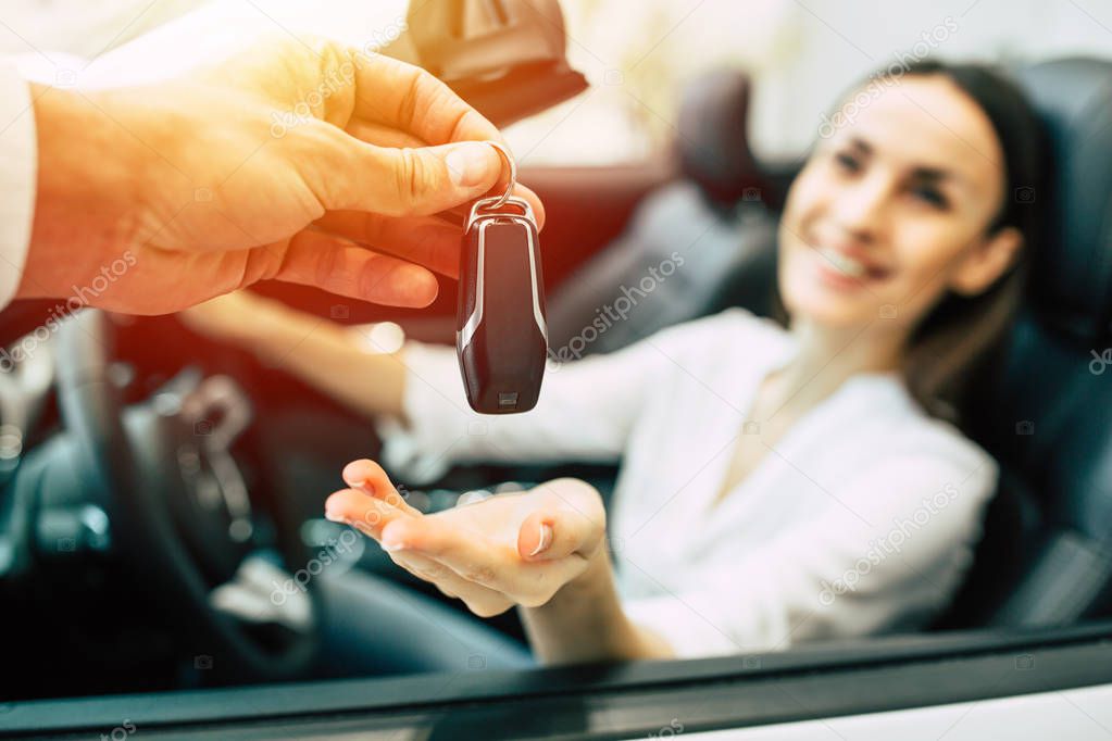 beautiful woman receiving key of new car from salesman in dealership