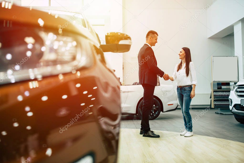 woman buying new car in dealership shaking hands with male consultant 