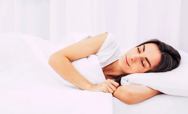 Όμορφη νεαρή μελαχρινή γυναίκα κοιμάται σε ένα λευκό κρεβάτι. — Φωτογραφία Αρχείου