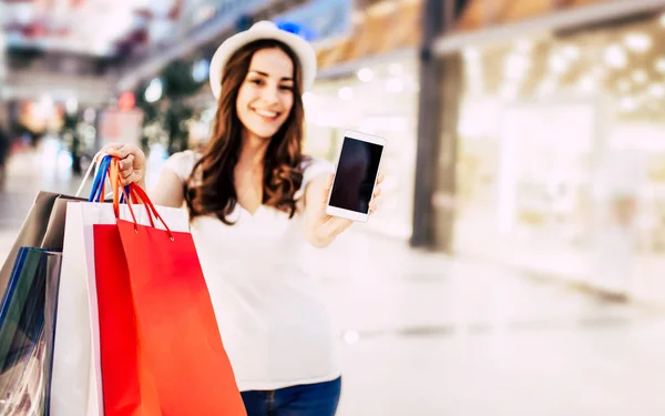 Žena s tašky ukazující telefon — Stock fotografie