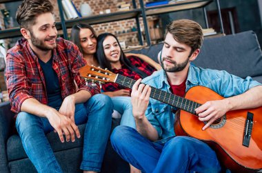 Grup Genç arkadaşlar evde rahatlatıcı ve adam gitar çalmak