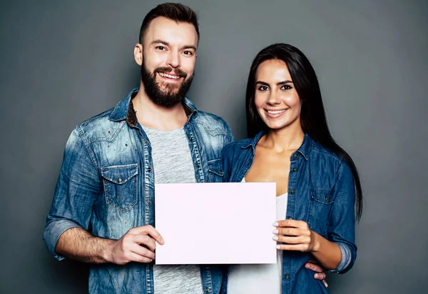 Junges Lächelndes Paar Mit Leerem Blatt Papier Vor Grauem Hintergrund — Stockfoto