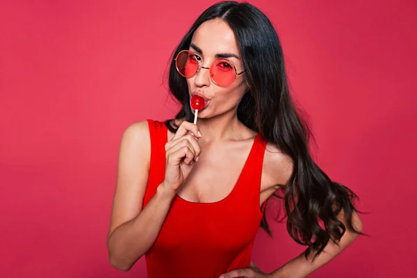 Young brunette woman with lollipop posing on red background
