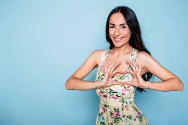 Genç esmer kadın elinde kalp ile mavi arka plan üzerinde poz şeklinde