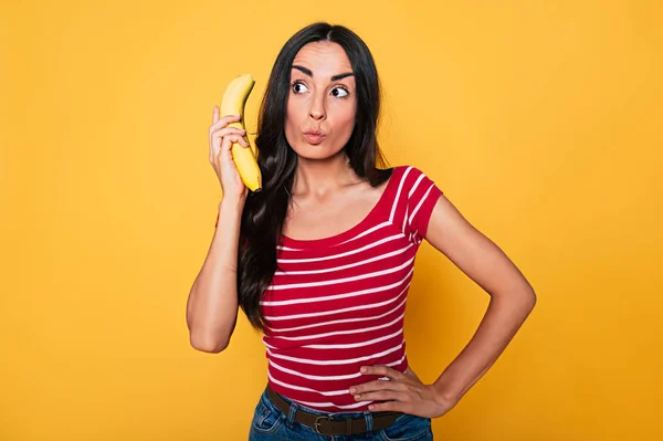 若いブルネット女性が黄色の背景にバナナのポーズ — ストック写真