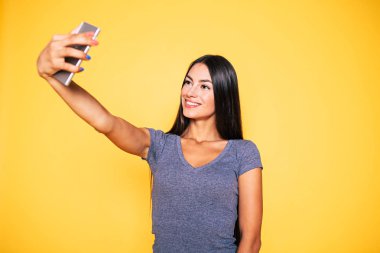 Smartphone üzerinde sarı arka plan kullanarak selfie yapma genç kadın portresi
