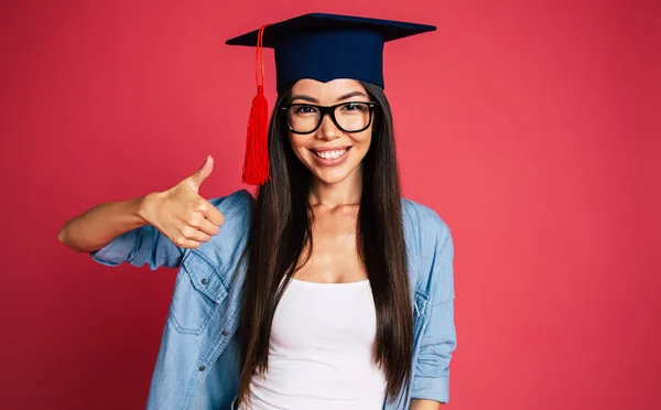 Portrait of young brunette posing in graduate hat on red background