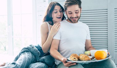 Yatakta kahvaltı ile oturan genç çift 