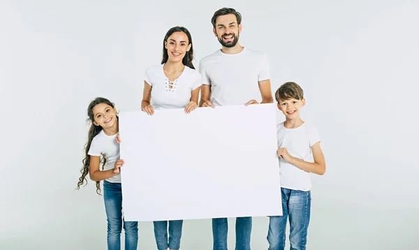 在白色背景的空白纸的年轻的幸福的家庭持有白色页 — 图库照片