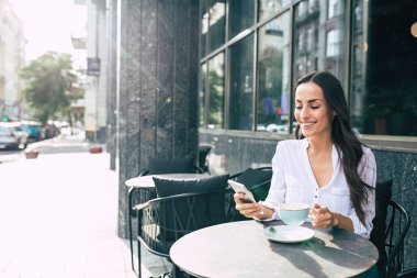 Smartphone kullanarak ve kahve içme genç gülümseyen kadın 