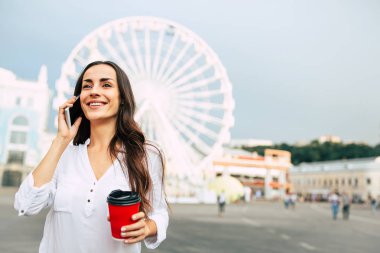 Smartphone kullanarak ve kahve içme genç gülümseyen kadın 