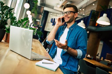 Notlar ve smartphone tarafından kafede dizüstü bilgisayarda çalışırken konuşmak genç adam 