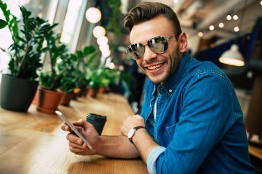 kafede otururken Smartphone kullanan genç adam