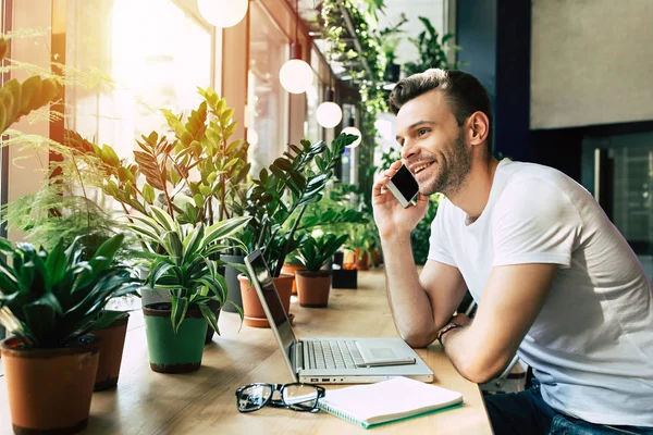 Joven Hablando Por Teléfono Inteligente Cerca Computadora Portátil Mientras Está — Foto de Stock