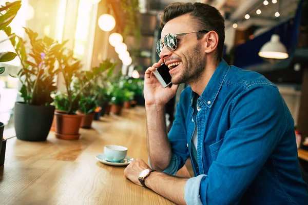 young man speaking by smartphone while sitting at cafe