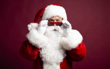 Noel Baba kostüm giyen güneş gözlüğü ve kırmızı zemin üzerine kameraya bakarak adam portresi Noel ve yeni yıl kavramı 