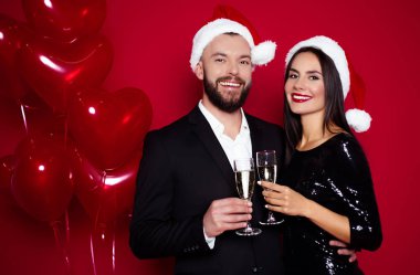 Kutluyor yeni yıl şampanya kırmızı arka plan ile şık çift Santa şapka