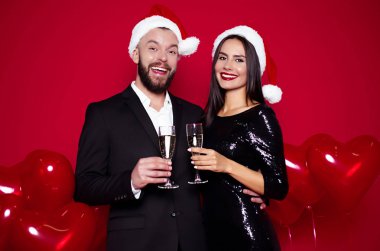 Kutluyor yeni yıl şampanya kırmızı arka plan ile şık çift Santa şapka