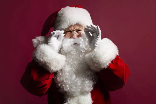 portrait of man in Santa Clause costume wearing glasses while posing on red background, Christmas and New year concept
