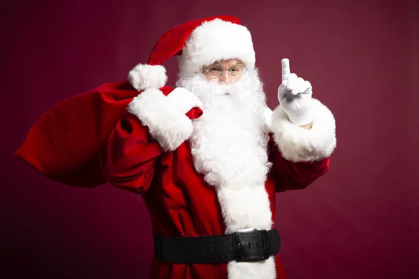 portrait of man in Santa Clause costume with gift sack on back showing idea sign on red background, Christmas and New year concept