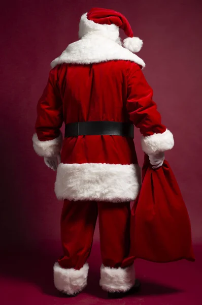 back view of man in Santa Clause costume holding gift sack on red background, Christmas and New year concept