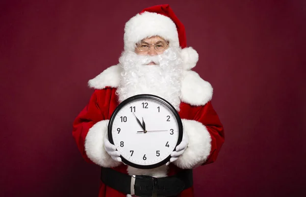 portrait of man in Santa Clause costume holding white clock on red background, Christmas and New year concept