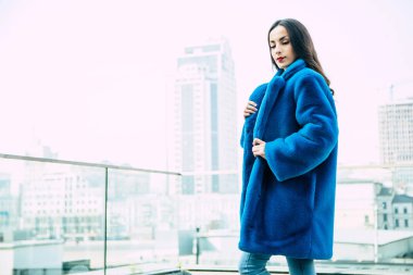 Genç kadın kentsel arka plan üzerinde poz mavi kürk ceket