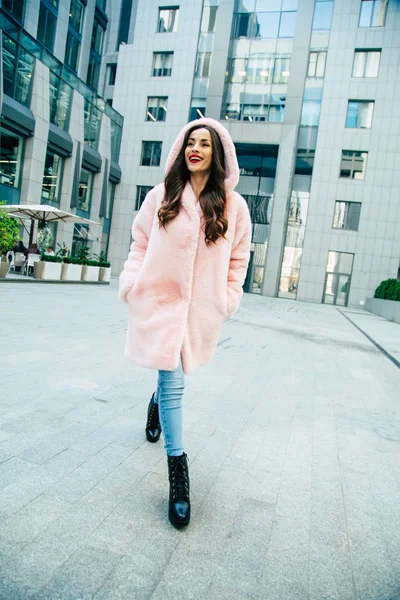 Young woman in pink fur coat walking by street